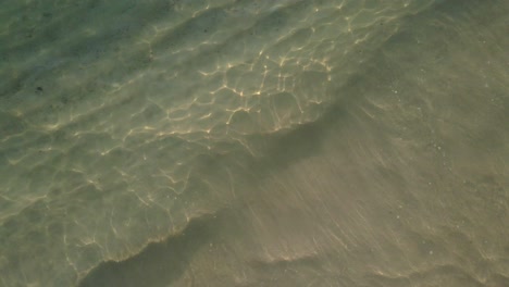 Aerial-top-view,-medium-rotating-spin-shot-of-sea,-small-tropical-wave’s-lap-on-a-beach