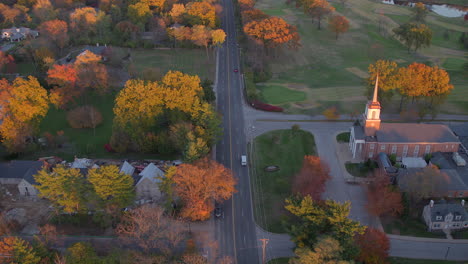 Aerial-pull-back-down-a-pretty-road-in-Ladue-and-away-from-a-church-and-houses-on-a-beautiful-Autumn-evening-at-golden-hour