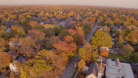 Aerial-push-over-beautiful-neighborhood-in-Kirkwood,-Missouri-in-Autumn-at-golden-hour-past-a-small-church-and-over-houses-and-trees