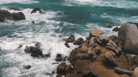 Waves-crashing-against-stack-of-rocks-in-the-blue-sea-of-Tayrona-Park,-Colombia