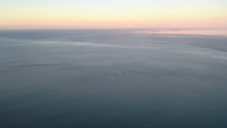 Aerial-tilt-up-from-turquoise-water-sea-to-beautiful-golden-hour-horizon-during-sunset
