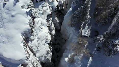 Aerial-view-of-snow-capped-cliffs-in-a-sunny-winter-landscape-of-Ouray-Ice-Park-Colorado-USA,-birdseye-tilt-down-drone-shot