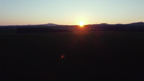 Sunset-above-green-fields-with-a-hill-on-the-horizon,-aerial-shot,-truck-left