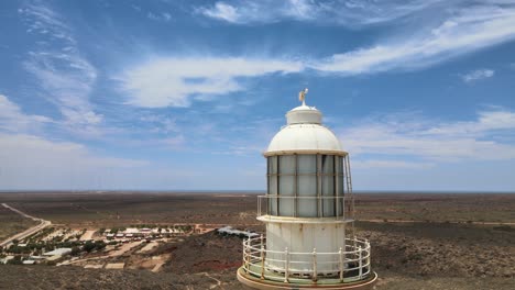 High-old-historical-lighthouse-at-a-hill-next-to-the-blue-In-Pacific-Ocean-on-a-partly-cloudy-day-near-Exmouth,-Western-Australia