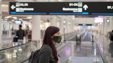 Tilt-down-from-airport-terminal-sign-to-woman-wearing-a-mask-on-a-moving-walkway