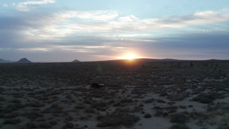 Einsamer-Jeep,-Der-Bei-Sonnenuntergang-Oder-Sonnenaufgang-Die-Mojave-Wüstenlandschaft-Hinunterfährt---Luftbild