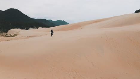Sandboarder-walking-on-sand-dunes-near-the-tropical-beach-of-Garopaba,-Santa-Catarina,-Brazil