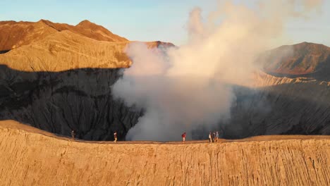 Golden-sunlight-shines-on-slope-of-Mount-Bromo,-active-volcano-in-Java,-people-walking-on-ridge