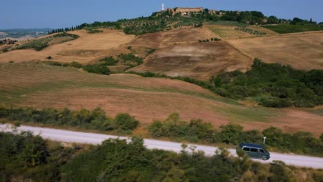 T4-VW-Volkswagen-hippie-Bulli-van-car-is-driving-along-a-road-at-Pienza-in-Val-d'-Orcia-valley-near-Siena-and-Florence-in-Tuscany,-Italy-with-wine-and-fields
