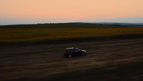 SUV-off-roading-near-sunflower-fields-in-the-evening,-drone-tracking-car