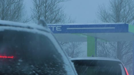 Busy-Neste-petrol-station-with-queues-of-people-refilling-their-cars-in-fear-of-fuel-shortages,-rising-prices,-hype-at-gas-stations,-overcast-winter-day-with-heavy-snowstorm,-medium-handheld-shot