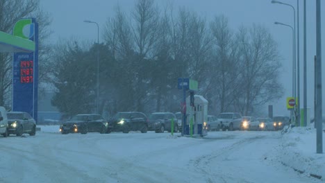 Busy-Neste-petrol-station-with-queues-of-people-refilling-their-cars-in-fear-of-fuel-shortages,-rising-prices,-hype-at-gas-stations,-overcast-winter-day-with-heavy-snowstorm,-medium-handheld-shot