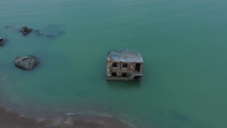 Aerial-birdseye-view-of-abandoned-seaside-fortification-building-at-Karosta-Northern-Forts-on-the-beach-of-Baltic-sea-,-waves-splash,-overcast-day,-wide-rotating-drone-shot