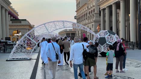 People-are-walking-in-the-old-fashioned-arch-architectural-design-buildings-pillar-stones-roman-medieval-towers-downtown-old-city-in-Doha-Qatar-football-decoration-at-dusk-sunset-in-autumn-middle-east