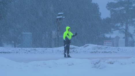 Oficial-De-Policía-Vial-Letón-Organizando-El-Tráfico-De-Automóviles-Durante-Una-Fuerte-Ventisca-De-Nieve,-Día-De-Invierno-Nublado,-Tiro-Medio-Distante-De-Mano