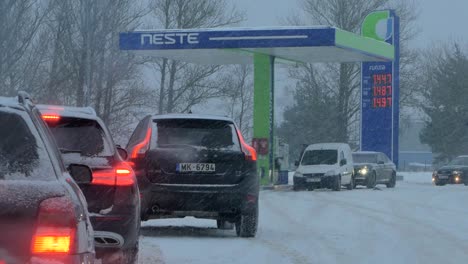 Busy-Neste-petrol-station-with-queues-of-people-refilling-their-cars-in-fear-of-fuel-shortages,-rising-prices,-hype-at-gas-stations,-overcast-winter-day-with-heavy-snowstorm,-medium-handheld-shot