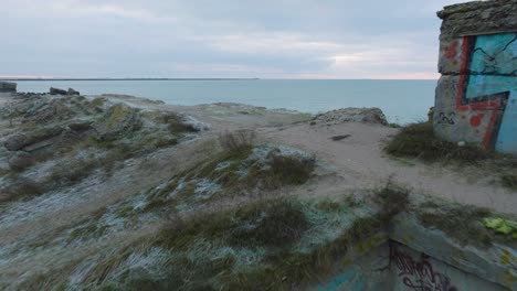 Establishing-aerial-view-of-abandoned-seaside-fortification-buildings-at-Karosta-Northern-Forts-on-the-beach-of-Baltic-sea-,-overcast-day,-wide-drone-shot-moving-forward