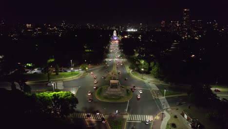 Aerial-view-of-the-Urquiza-Monument-at-night-with-the-main-avenue-with-constant-car-traffic,-Palermo,-Buenos-Aires,-Argentina