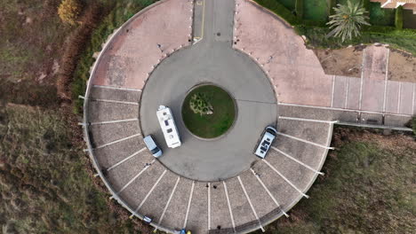 Motor-home-camper-van-circling-roundabout,-top-down-descending-aerial-view