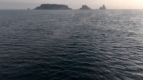 Aerial-view-flying-across-Mediterranean-sea-waves-tilt-up-reveal-of-Medes-islands-in-sunrise-horizon