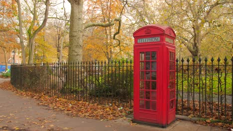Klassische-Rote-Telefonzelle-In-London-Mit-Gefallenen-Herbstblättern-Auf-Dem-Boden