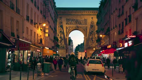 Crowd-of-people-walking-in-Rue-Saint-Denis-stores-on-the-sides,-the-Porte-Saint-Denis-named-after-Ludovico-Magno,-10th-arrondissement,-Paris,-France