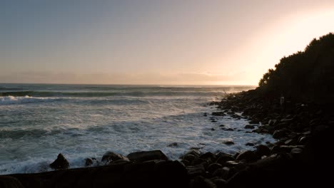 Waves-breaking-with-a-man-fishing-at-sunrise-at-Burleigh-Heads-on-the-Gold-Coast,-Queensland,-Australia