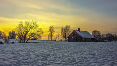 Timelapse-View-Of-Golden-Sun-Setting-On-Horizon-Over-Lone-Wooden-Barn-On-Snow-Covered-Landscape