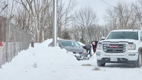 People-in-the-street-clearing-snow-next-to-a-car,-After-Winter-Snow-blizzards,-Canada