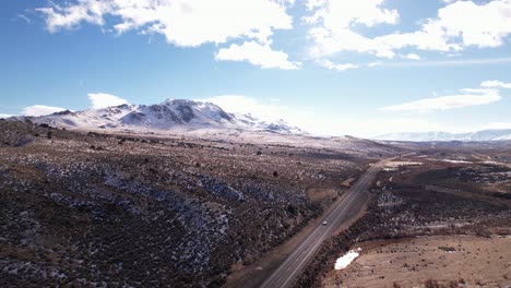 Vista-Aérea-De-La-Pintoresca-Carretera-Solitaria-Con-Autos-Que-Conducen-Rápido-Y-El-Paisaje-Montañoso-Del-Pico-Nevado-Sierra-Nevada-California