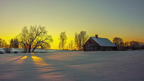 Time-lapse-shot-of-golden-sunset-behind-leafless-trees-and-snowy-farm-house-fields-in-the-evening---Beautiful-nature-scene-during-winter-with-blue-hour-and-purple-colored-sky