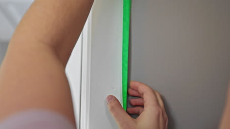 Close-up-of-a-white-woman-applying-green-painters-tape-along-the-edge-of-a-door-frame