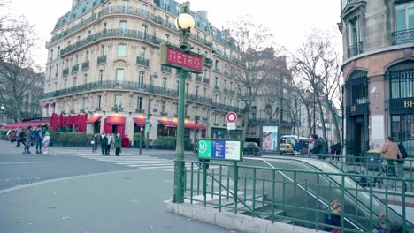 People-entering-the-metro-station,-Haussmannian-architecture-and-restaurant-in-the-background