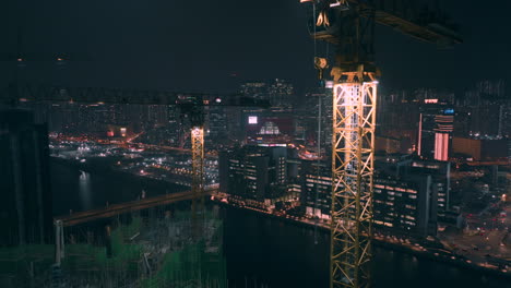 Aerial-backwards-shot-of-construction-site-crane-with-worker-climbing-down-at-night
