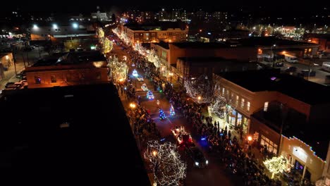 Wide-aerial-drone-shot-flying-over-brightly-lit-holiday-Christmas-parade-at-night