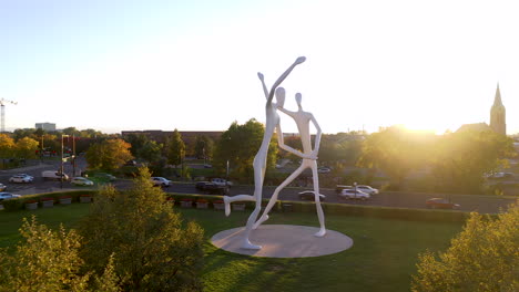 Escultura-De-Bailarines-En-El-Centro-De-Artes-Escénicas-De-Denver,-Monumento-De-La-Estatua-Contemporánea-Urbana-Al-Aire-Libre-En-El-Parque-Al-Atardecer-Junto-Al-Tráfico-De-Carreteras-Y-Automóviles