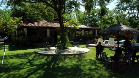 Slider-Shot-Of-People-Sitting-Together-In-Rest-House-Yard,-Enjoying-Summer-Time