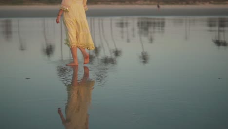 up-close-woman-in-a-yellow-dress-calmly-walking-barefoot-and-swinging-her-arms-at-the-shoreline-at-dawn