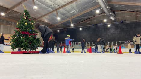 Vista-Estática-De-ángulo-Bajo-De-Muchos-Niños-Patinando-Sobre-Hielo-En-Una-Pista-Cubierta-En-Navidad-En-Majadahonda,-Madrid