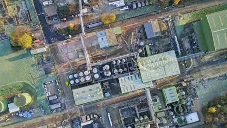 Slow-moving-overhead-aerial-footage-of-a-large-industrial-plant-showing-pipework-structures,-buildings,-cooling-towers,-steam,-and-work-vehicles