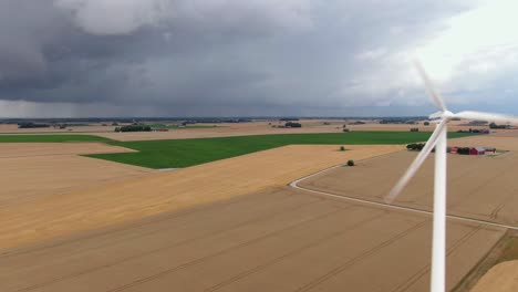 Dolly-drone-shot-of-vast-fields-in-southern-Sweden-with-wind-turbine-in-foreground