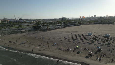 Drohnenvideo-Eines-Sommertages-An-Einem-Strand-In-Valencia,-Spanien,-Mit-Zwei-Flaggen-Im-Hintergrund