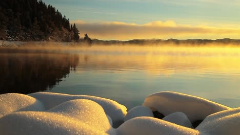Orange-sunrise-light-and-flowing-fog-over-freezing-surface-of-Jonsvatnet-lake-in-Norway