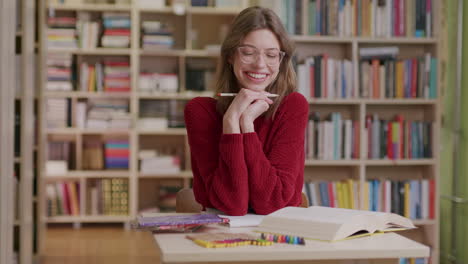 A-young-beautiful-female-student-smiles-into-the-camera-while-studying-in-the-library—medium-shot