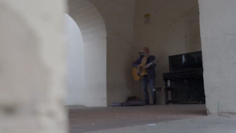 Matera,-Italy-Street-performer-playing-guitar-straight-on-with-piano-next-to-him-side-view-rack-focus-low-view