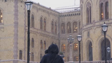 Gente-Caminando-Frente-Al-Edificio-Del-Parlamento-Noruego-En-El-Fondo-Durante-Las-Fuertes-Nevadas