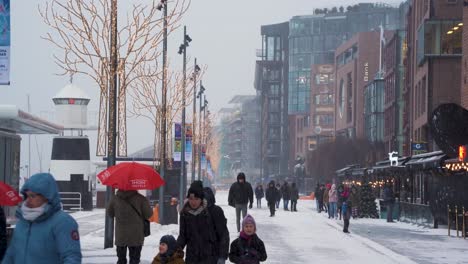 People-And-Families-Walking-Along-The-Promenade-At-Aker-Brygge-In-Oslo-During-Winter-And-Snow-Falling