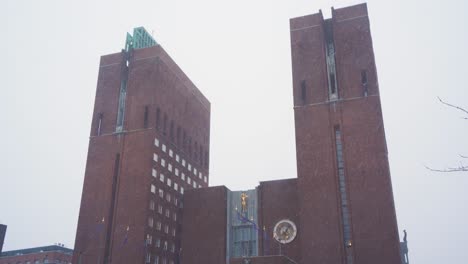 Blick-Auf-Das-Rathaus-Von-Oslo-An-Einem-Bewölkten,-Bewölkten-Wintertag-Mit-Schnee,-Der-Mit-Einer-Vorbeigehenden-Person-Fällt