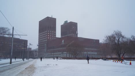 Rathaus-Von-Oslo-An-Bewölktem,-Bewölktem-Wintertag-Mit-Fallendem-Schnee-Und-Passanten,-Die-Von-Radhusplassen-Aus-Gesehen-Wurden