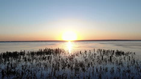 Fliegen-Auf-Dem-Goldenen-Sonnenaufgang-Mit-Spiegelreflexion-Auf-Einem-Ruhigen-See